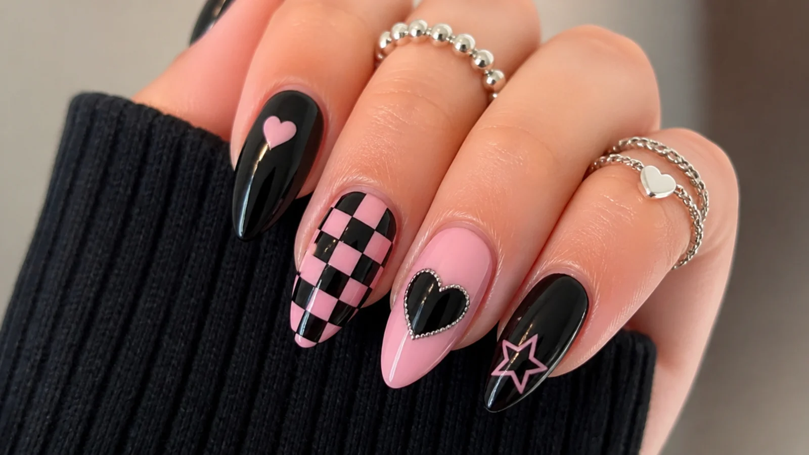 Black and pink emo nails with checkerboard and heart accents on almond shape