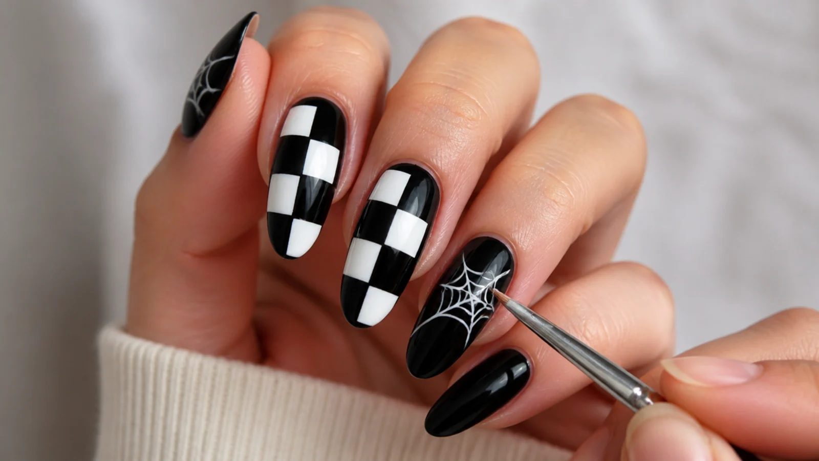 A thin brush painting a white checkerboard and a corner spiderweb on black nails