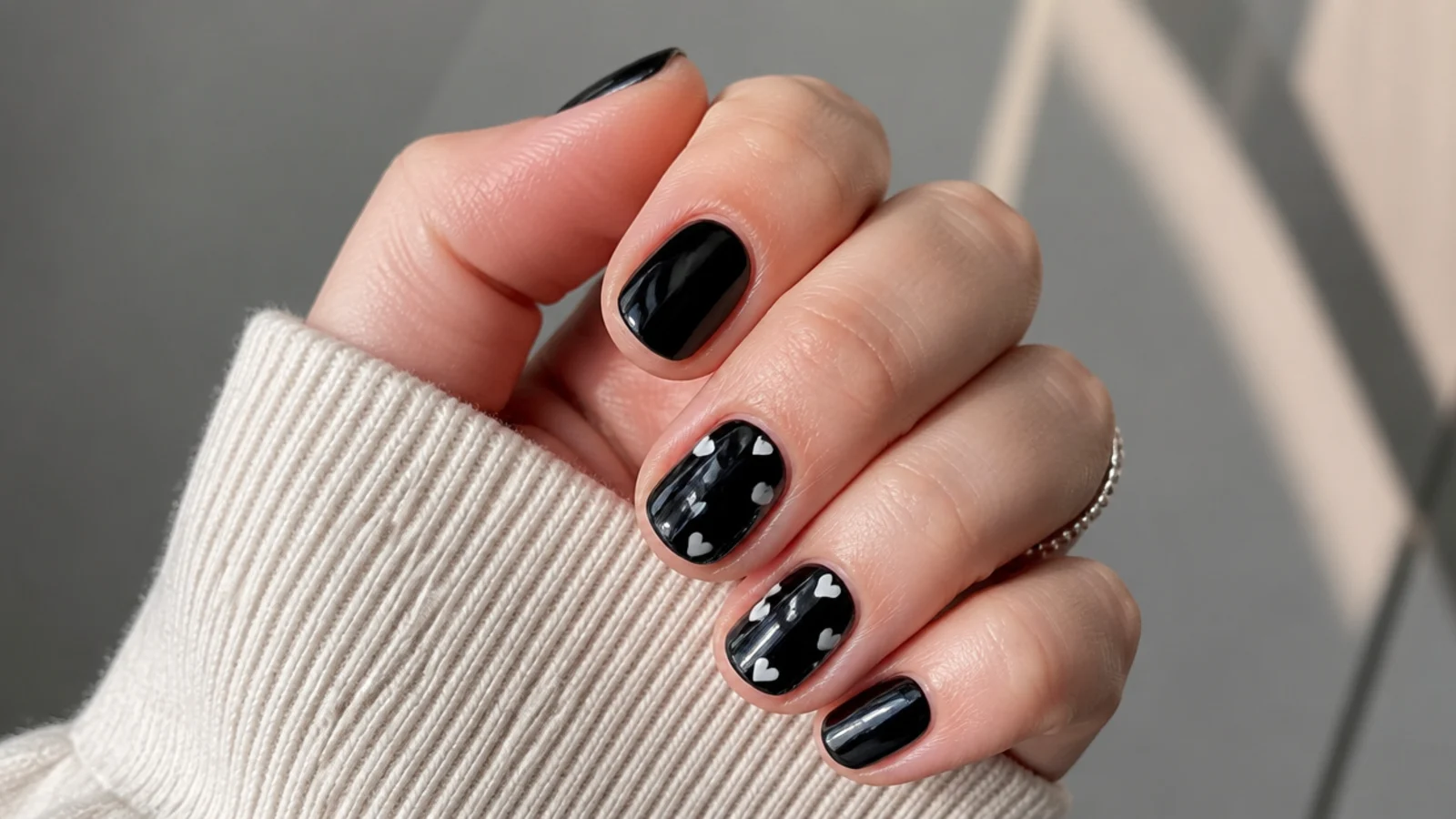 Short black nails with small white hearts scattered on two nails