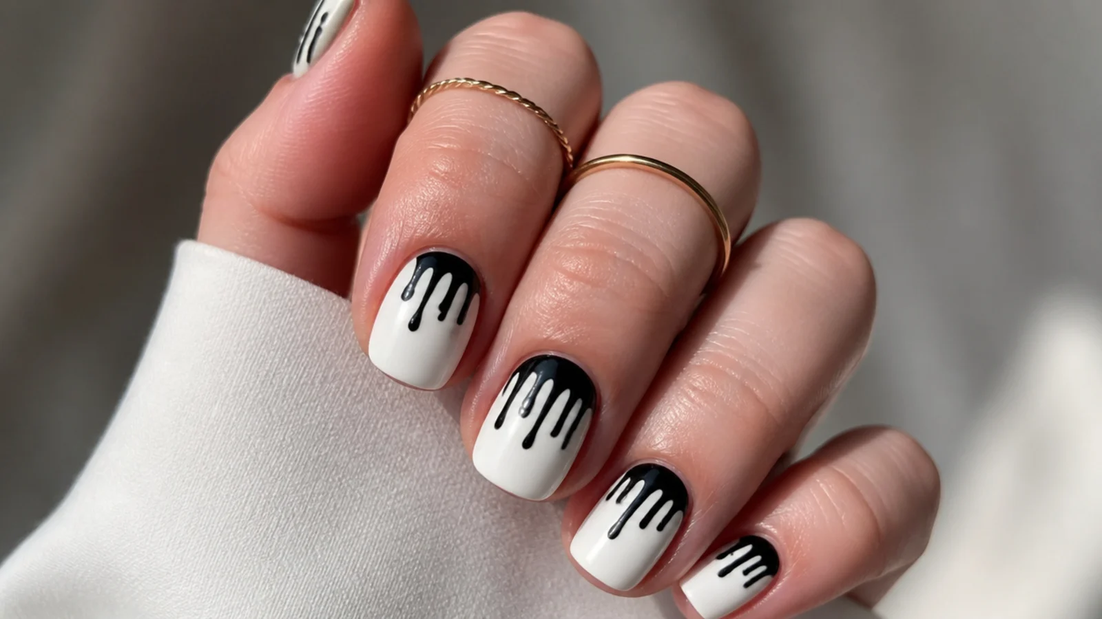 Short white nails with black paint drips coming down from the tips