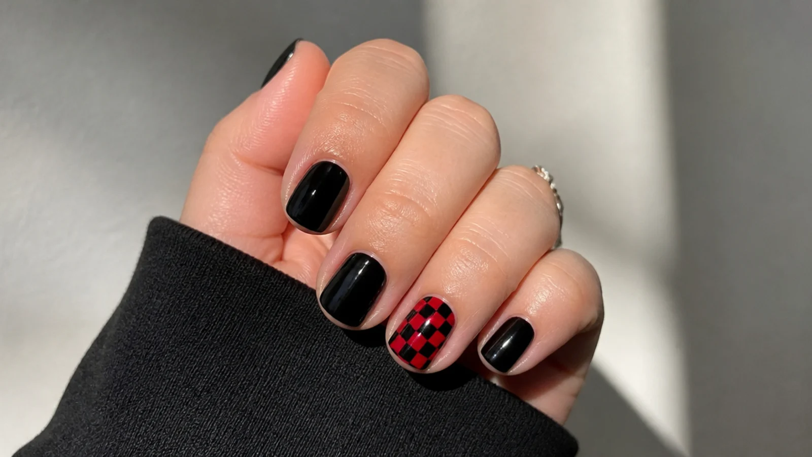 Short black nails with one red and black checkerboard accent nail