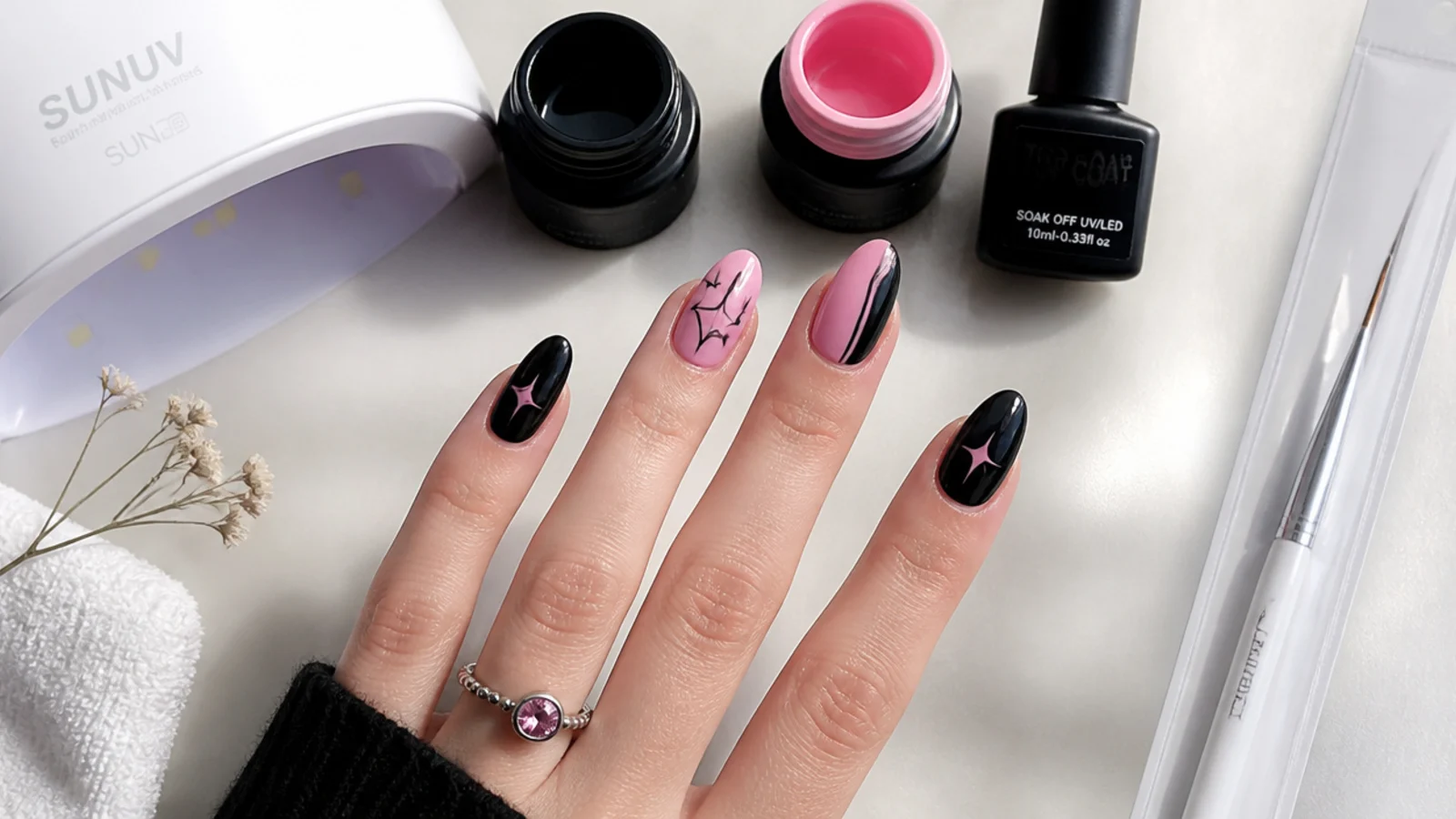 Flat lay of black and pink gels, liner brush, lamp and top coat for emo nails