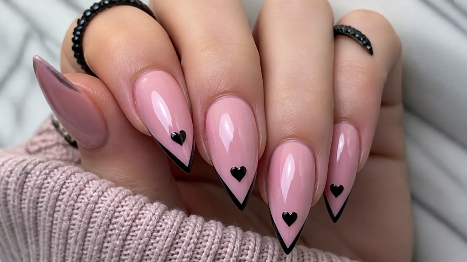 Soft pink emo nails with small black hearts near the tips