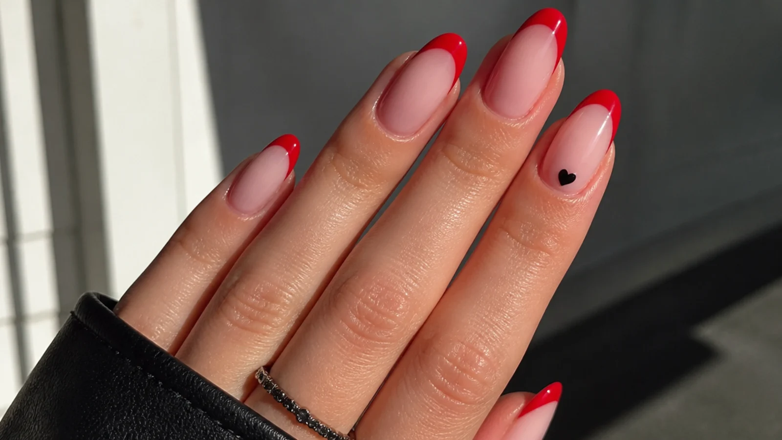 Nude emo nails with red French tips and a small black heart accent
