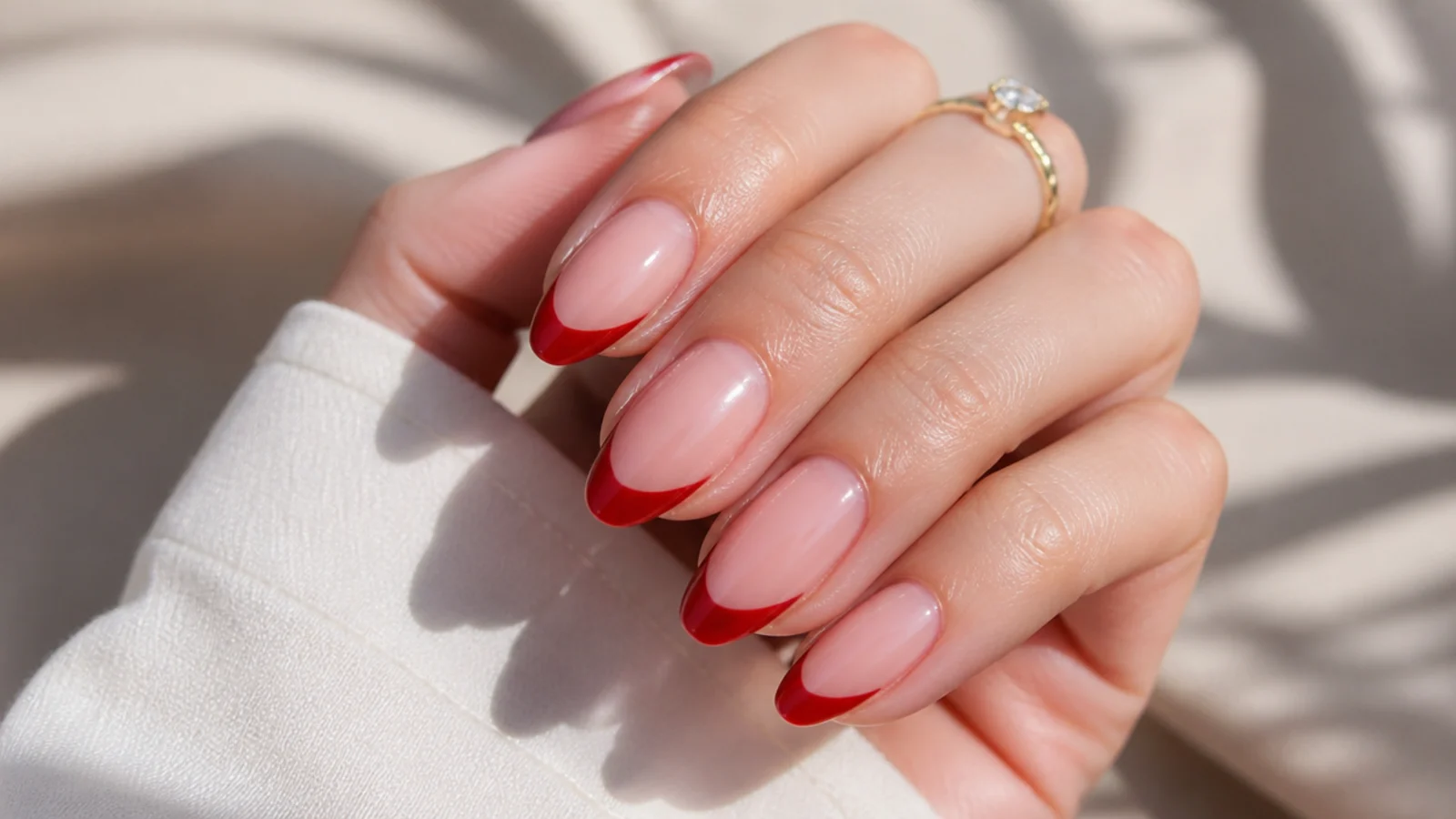 Almond nails with a glossy cherry red French tip over a sheer nude base