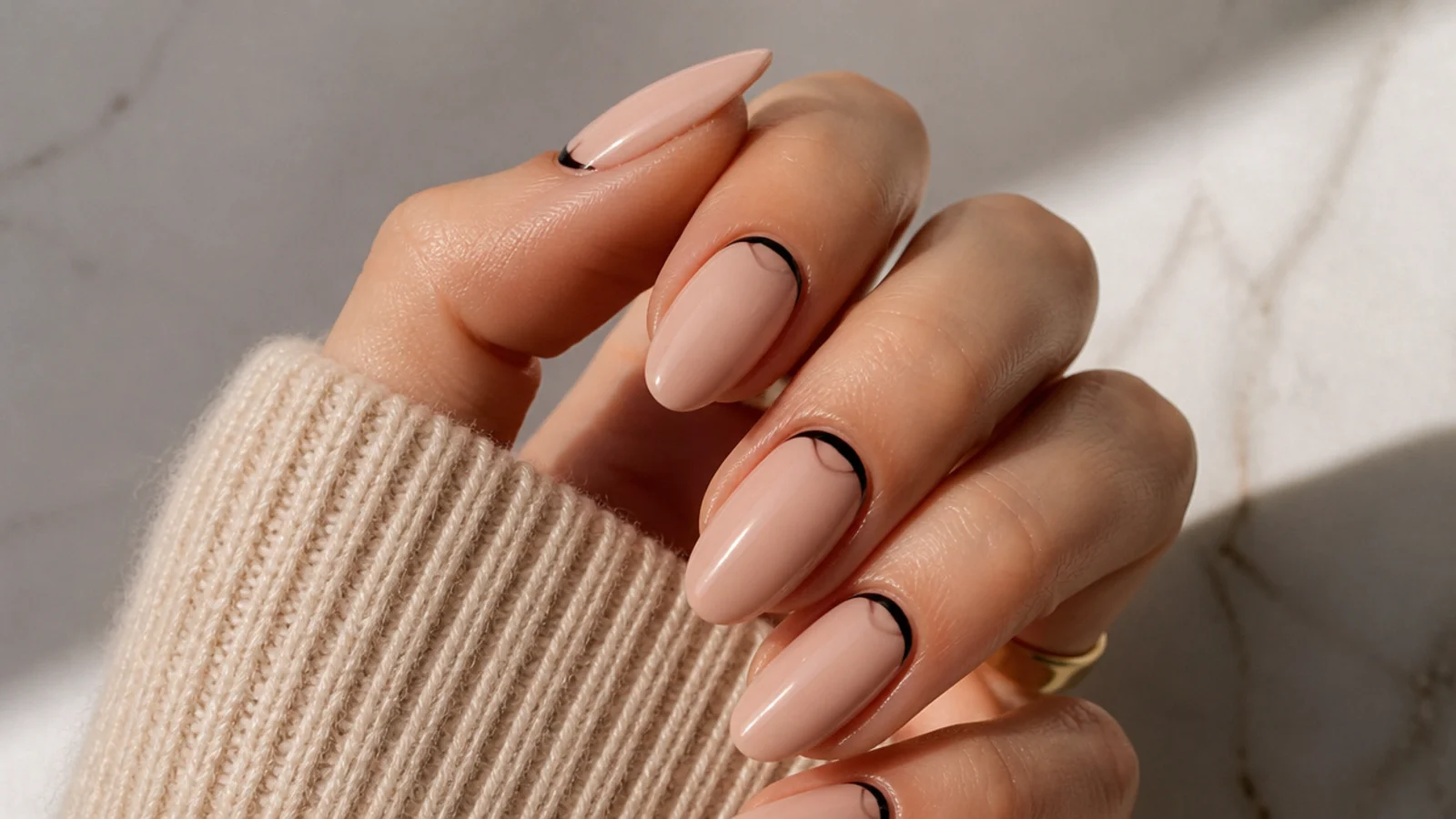 Nude almond nails with a reverse black French curve painted along the cuticle line