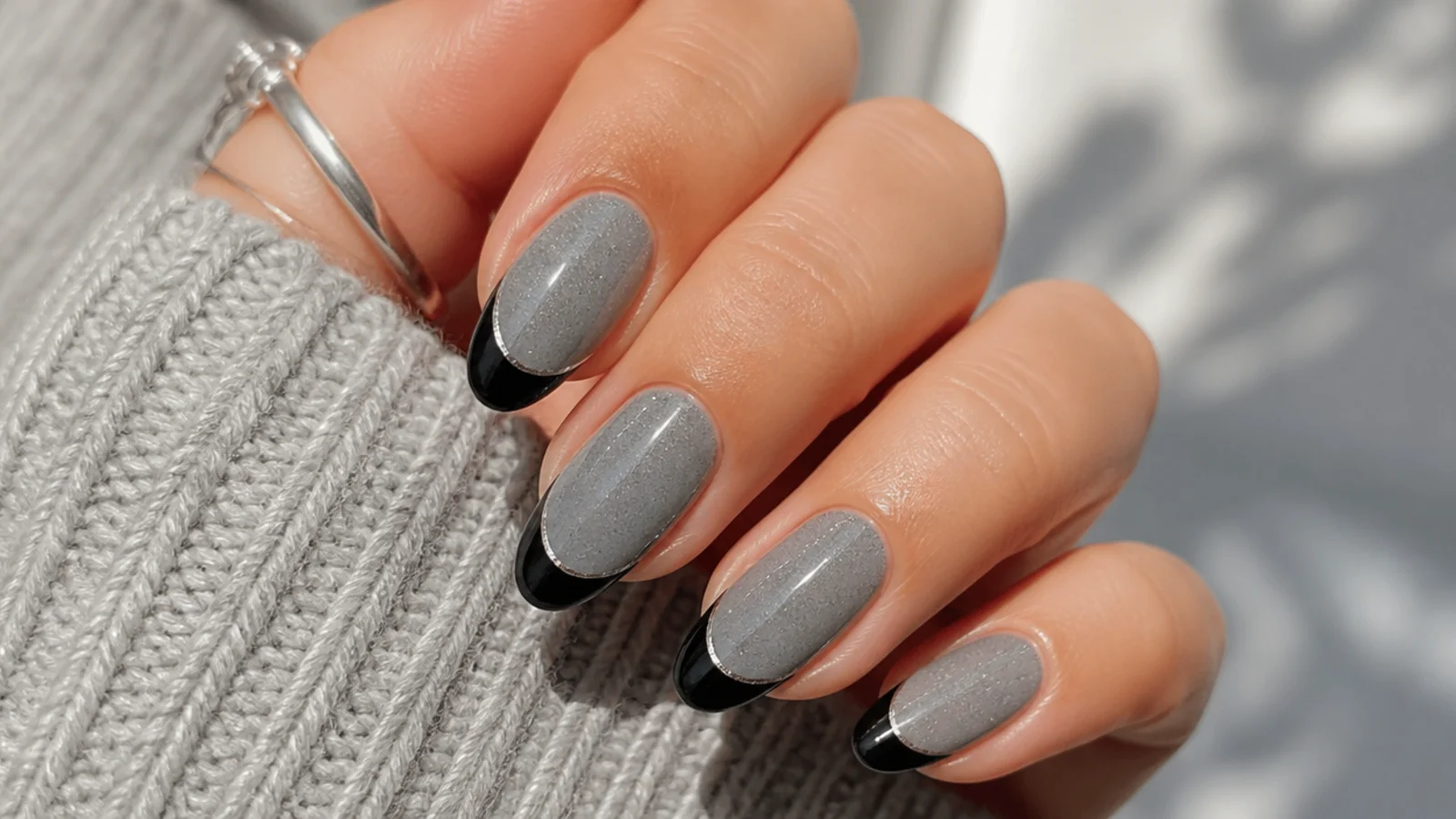 Almond nails with black French tips outlined by a fine silver line over a gray shimmer base
