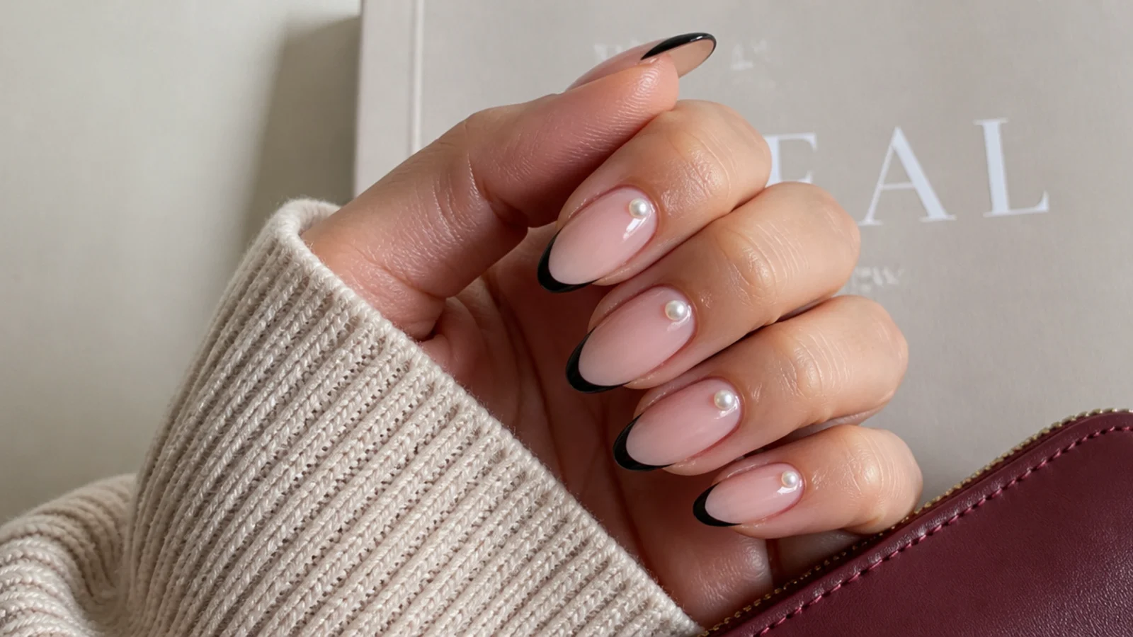 Almond nails with black French tips and small white 3D pearls set near the cuticle