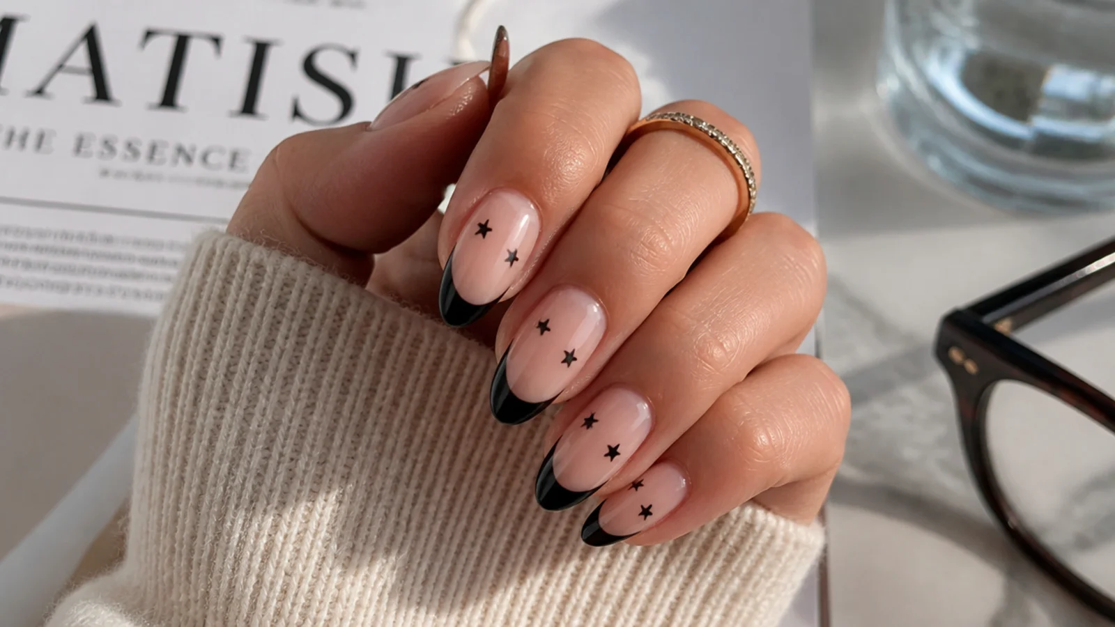 Almond nails with black French tips and tiny black five-point stars scattered on the nail bed