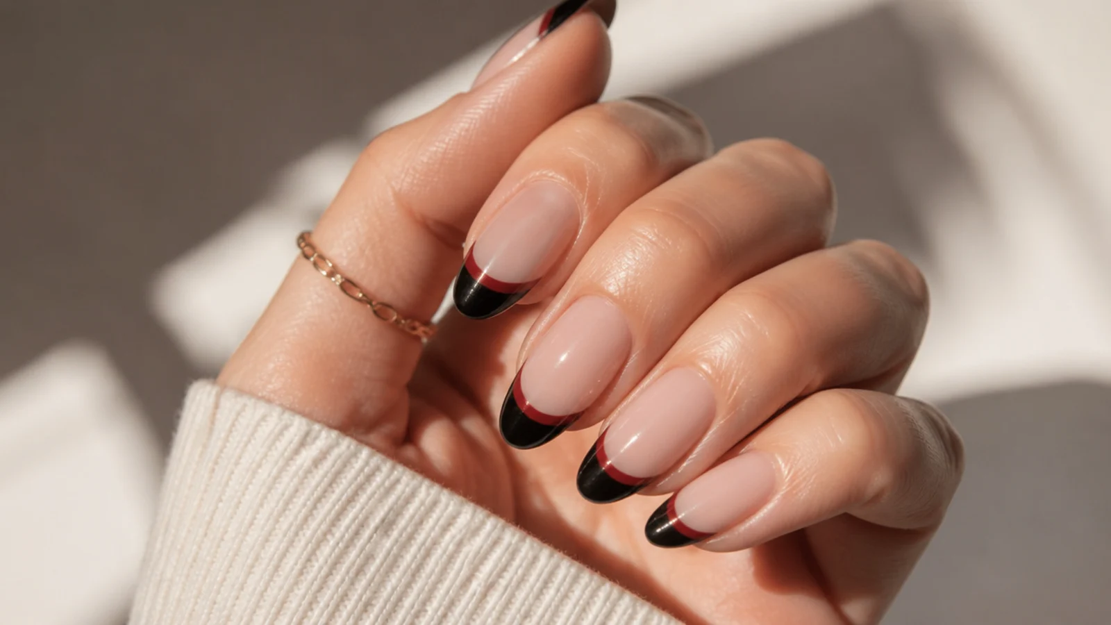 Almond nails with a black French tip and a thin blood red underline over a nude base