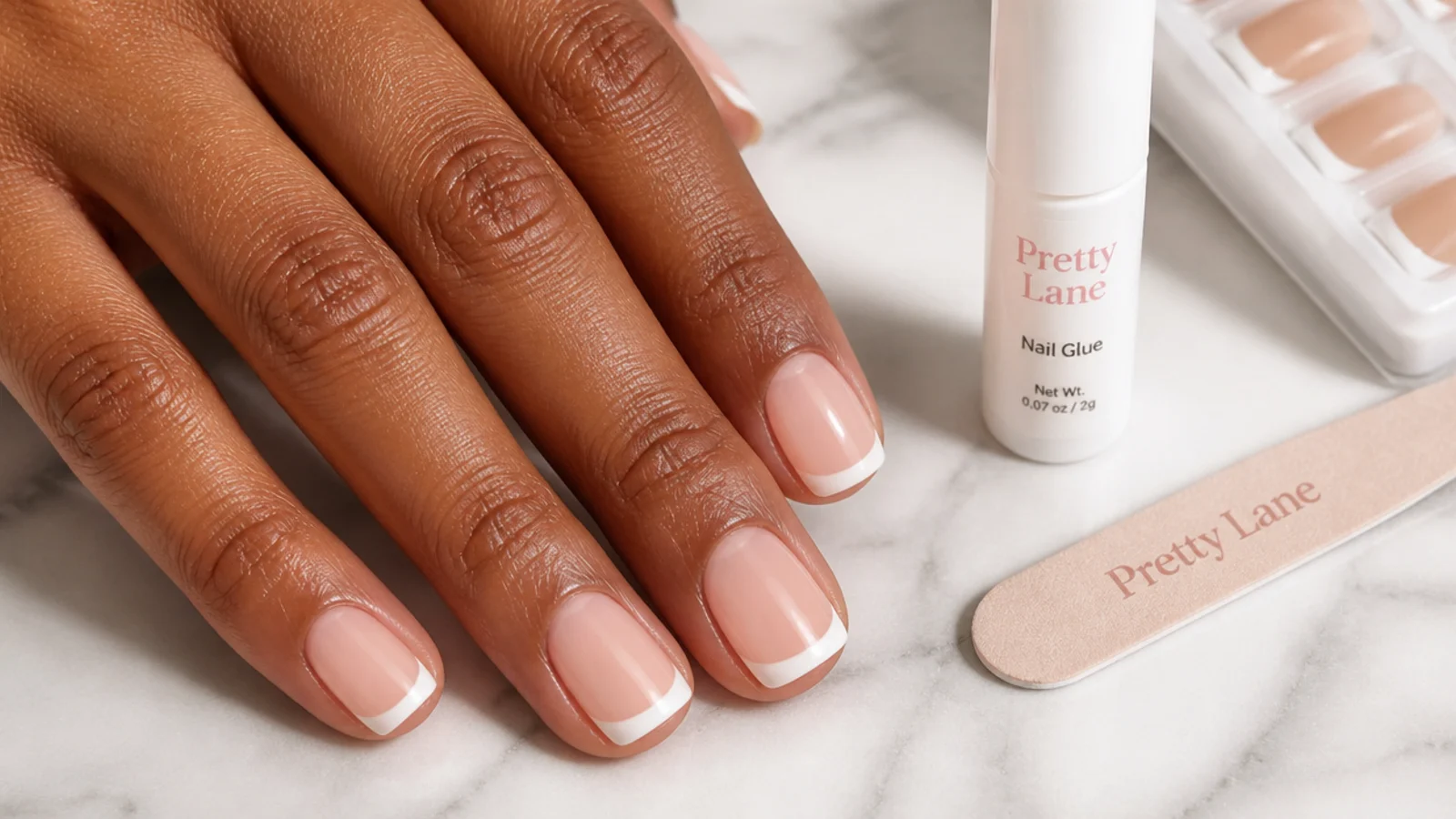 Short square French tip press-on nails with a thin white smile line beside nail glue and a mini file