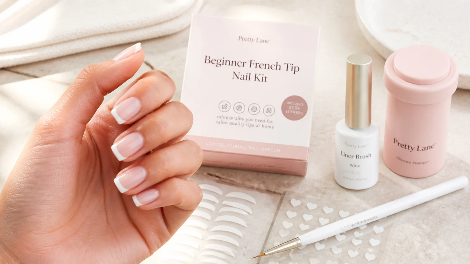 Beginner French tip nail kit laid out with a silicone stamper, liner brush, guide stickers and white gel polish