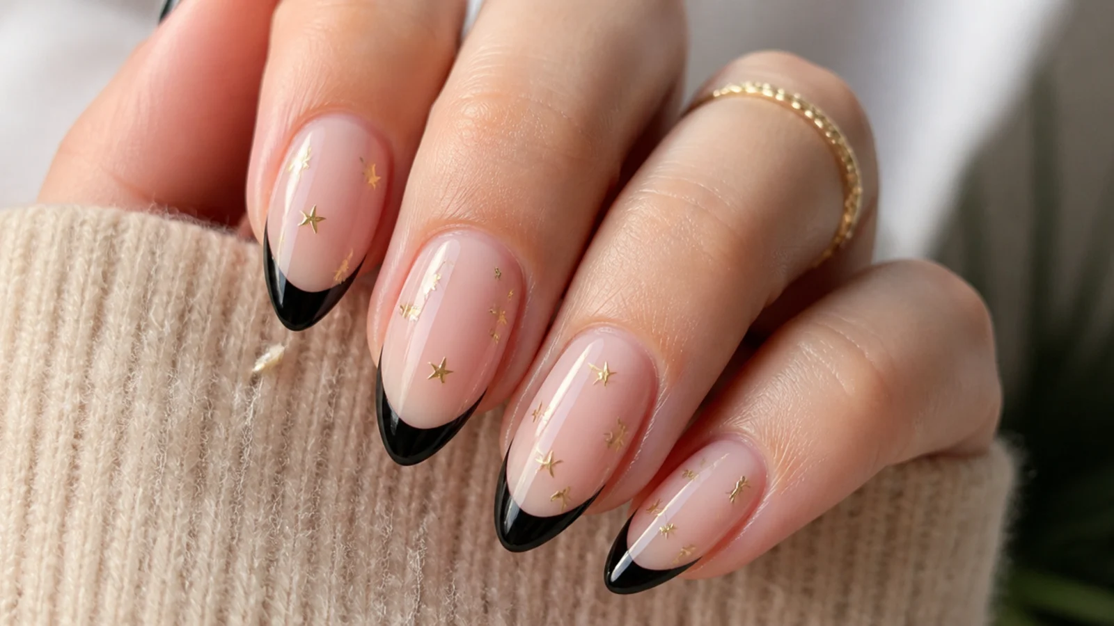 Almond nails with black French tips and small gold five-point stars scattered above the smile line