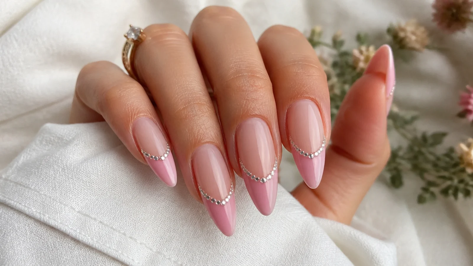 Long pink French tip nails with tiny clear rhinestones set along the smile line