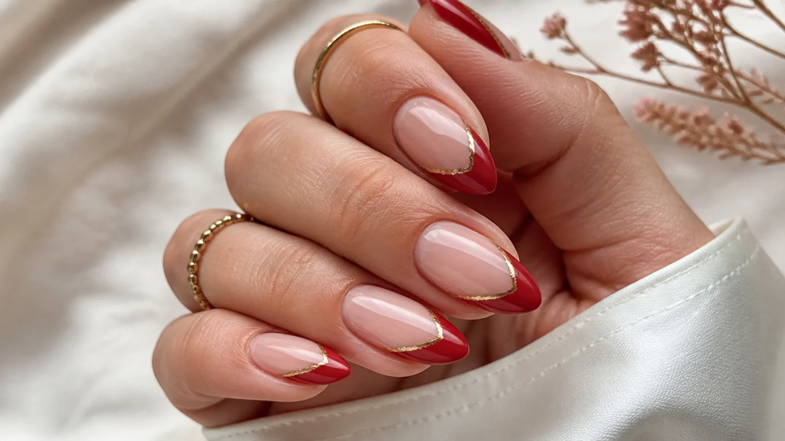 Medium almond nails with red French tips edged by a thin gold foil line on a nude base