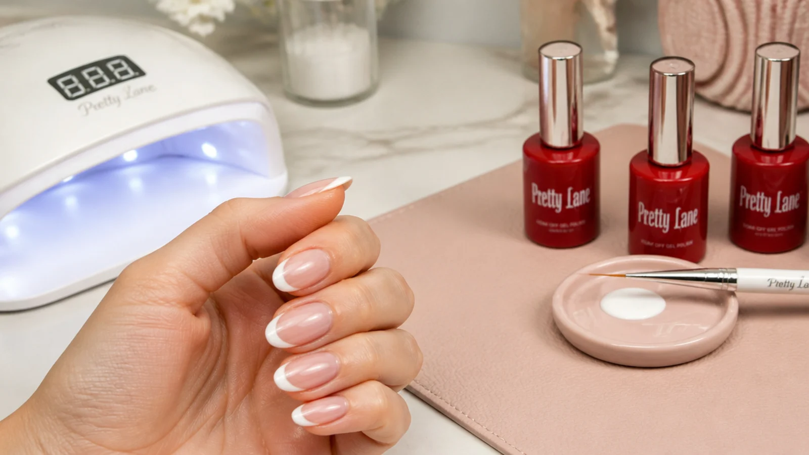 Nail salon station with red gel polish bottles, liner brush and lamp set up for a French tip