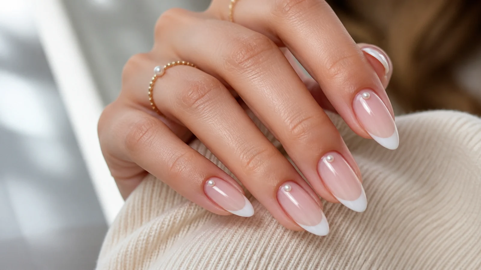 Long almond nails with white French tips and tiny half pearls placed near the cuticle