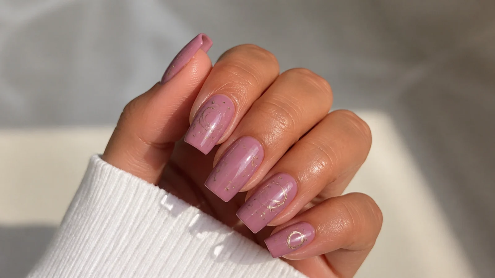 Warm pink-lavender acrylic nails in a squoval shape on tan skin