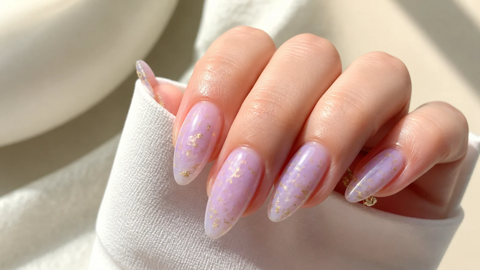 Milky lavender nails with thin gold foil flakes on an almond shape