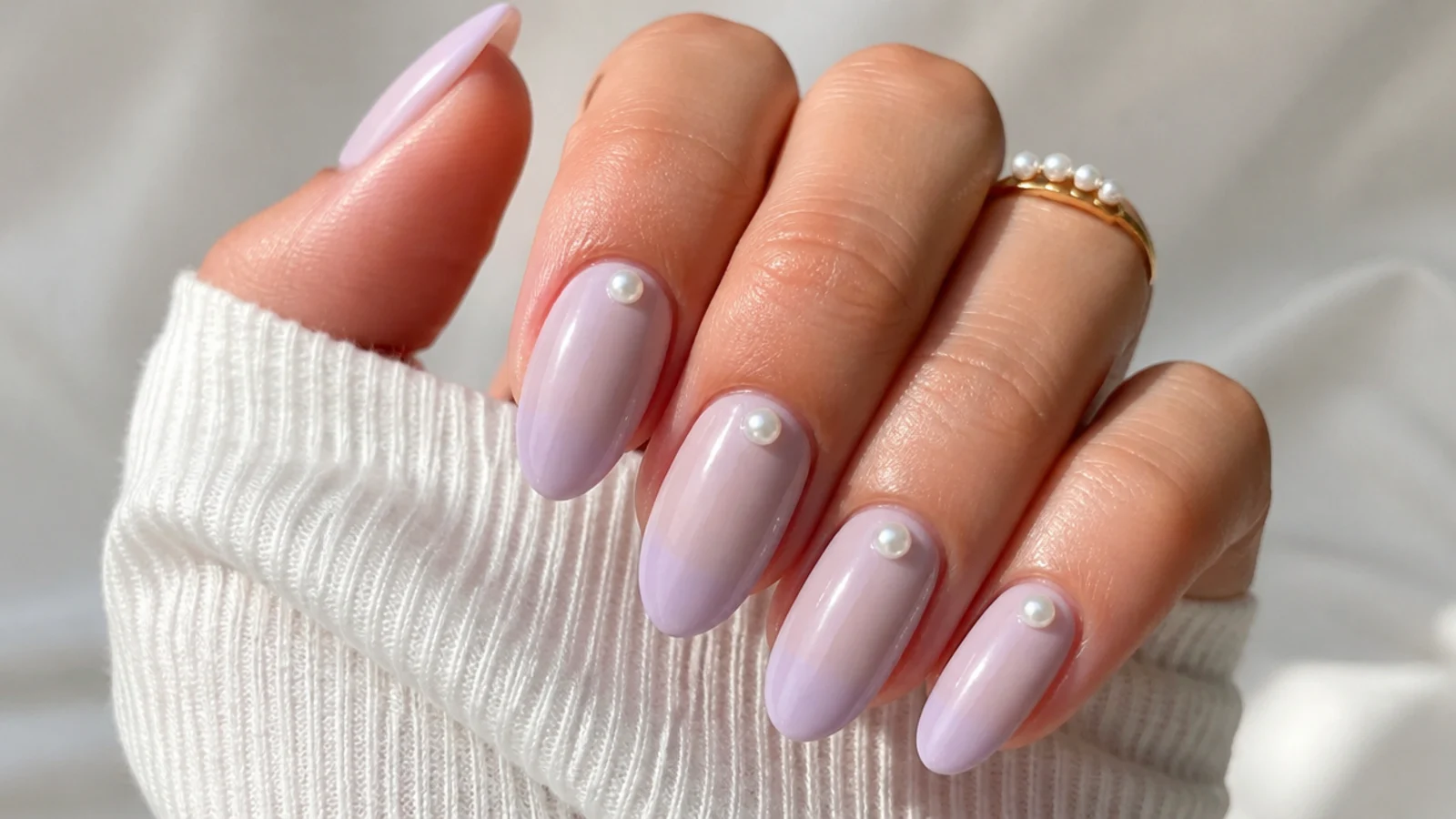 Milky lavender nails with small white pearl accents near the cuticle, almond shape