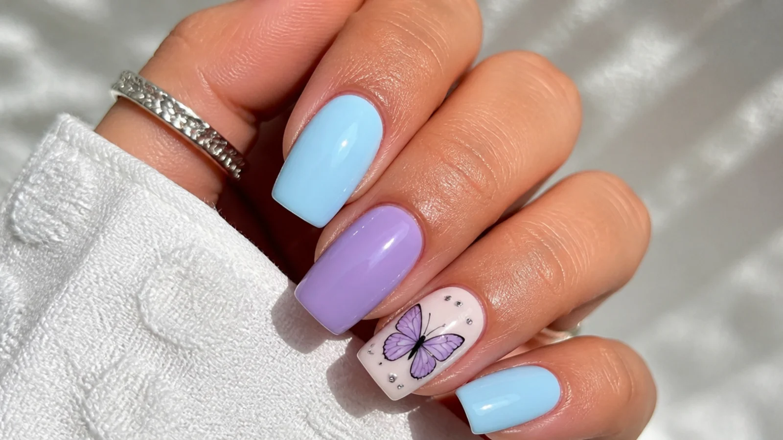 Pastel blue and purple nails with a small butterfly accent
