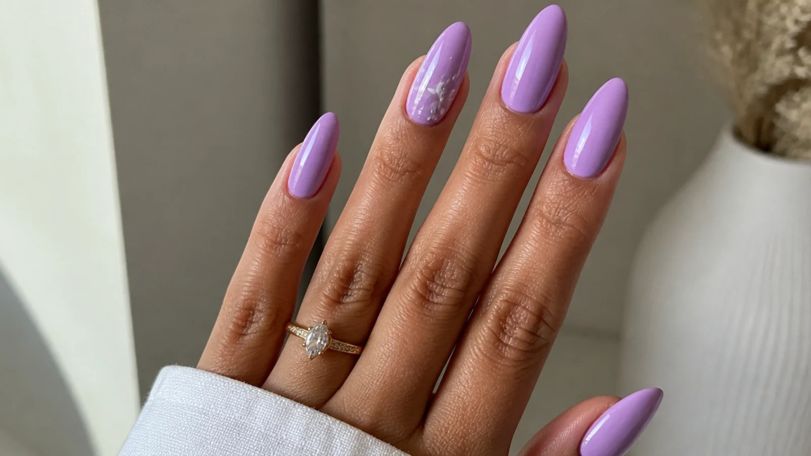 Warm pink-toned lilac acrylic nails on a tan hand, almond shape