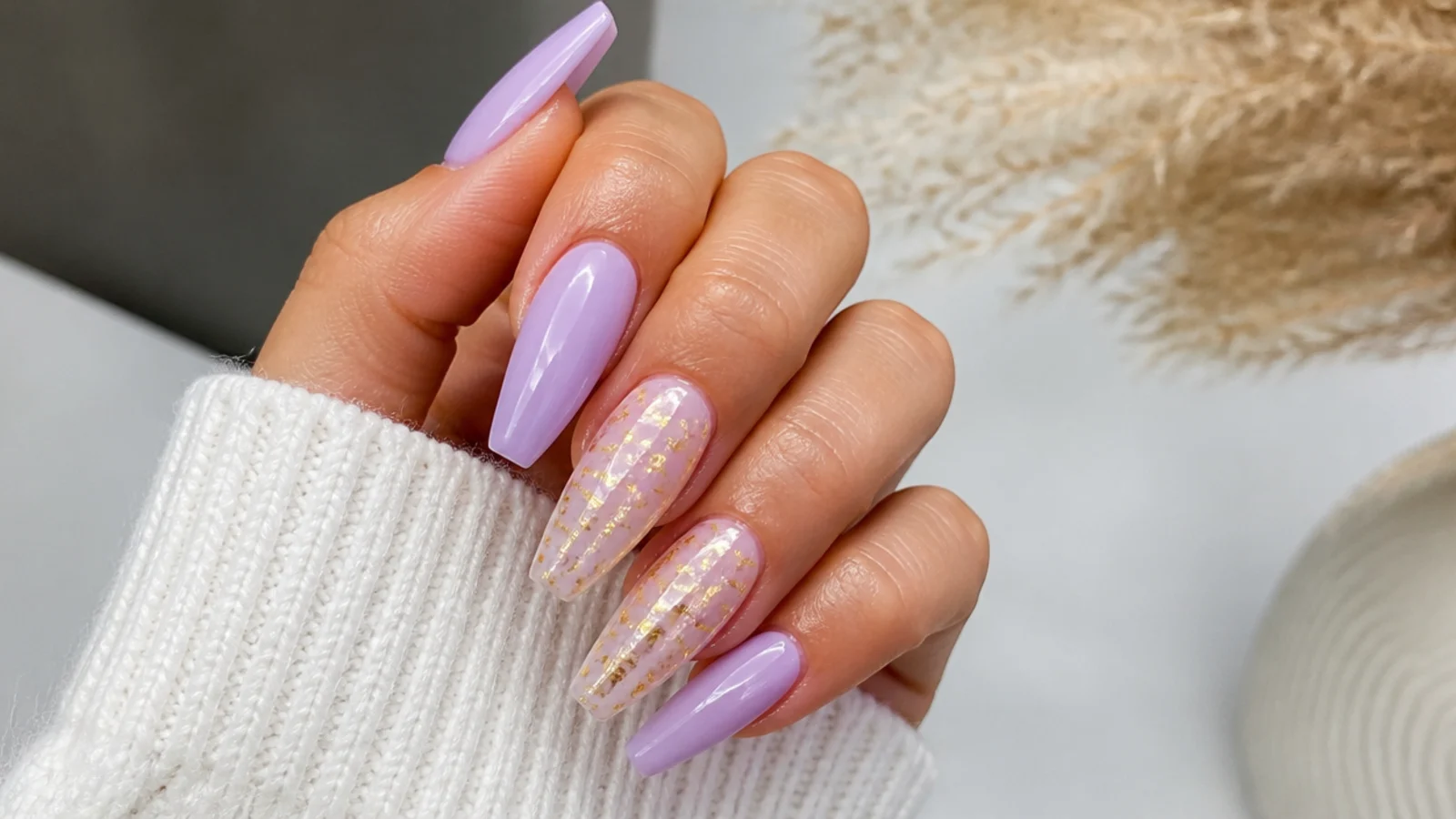 Warm light purple nails with gold glitter accents on a coffin shape