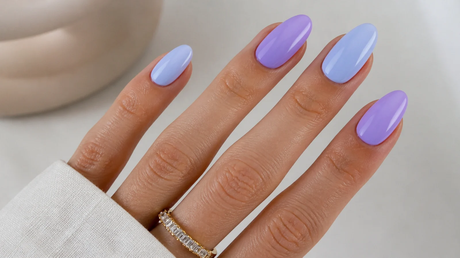 Alternating light purple and light blue pastel nails on a hand