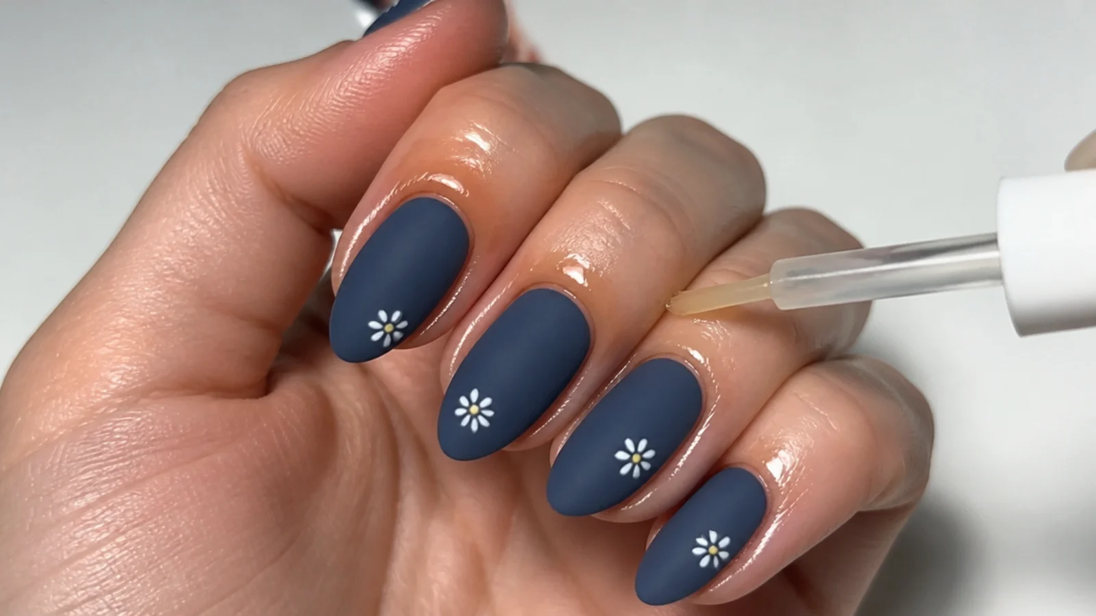 Cuticle oil applied around not across a matte blue nail to keep it flat