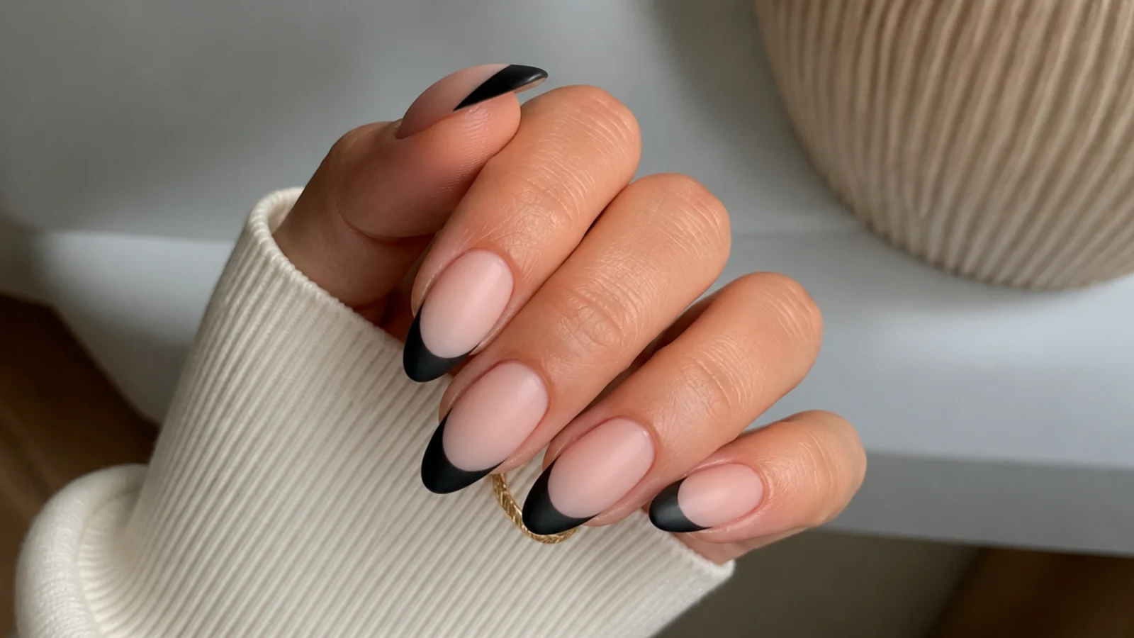 Nude nails with matte black French tips on an almond shape
