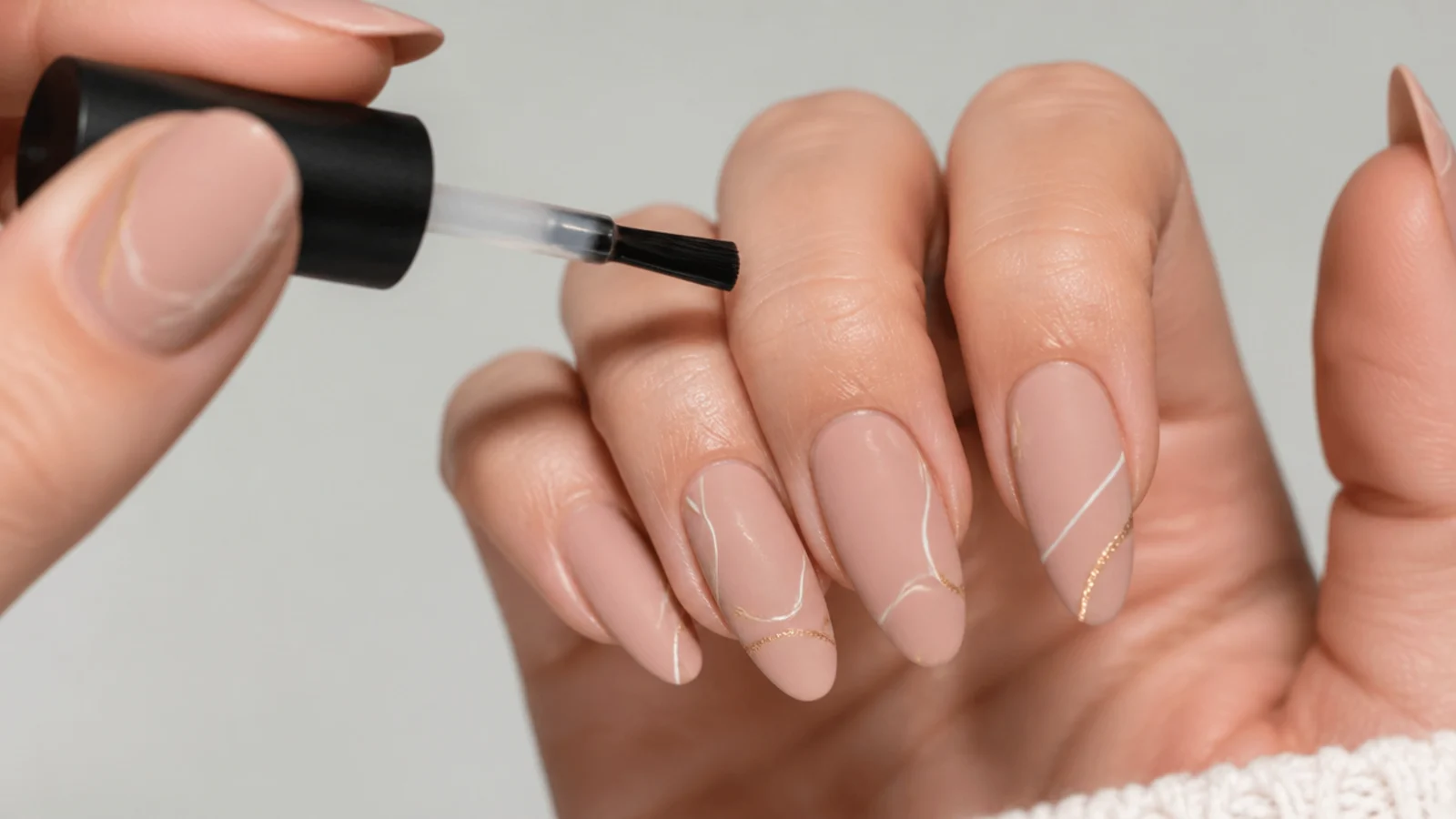 A matte gel top coat being brushed over a cured nude gel nail