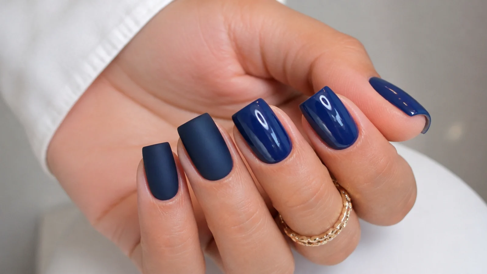Matte navy blue nails beside glossy blue nails on a square shape