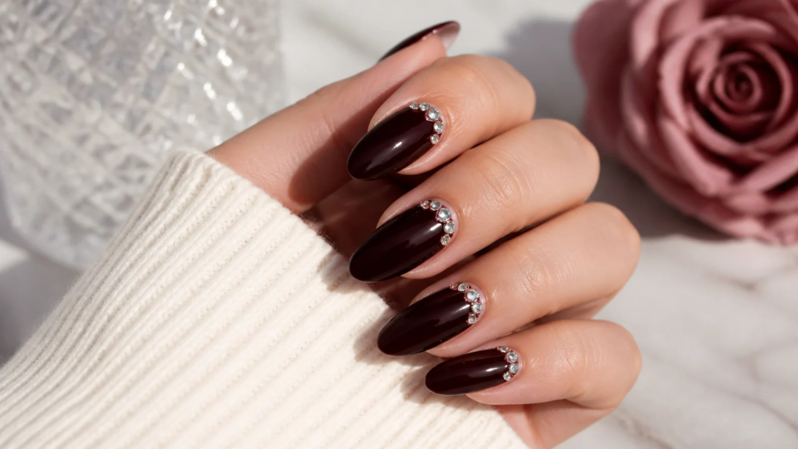 Long almond nails in glossy burgundy with a cluster of small crystals near one cuticle