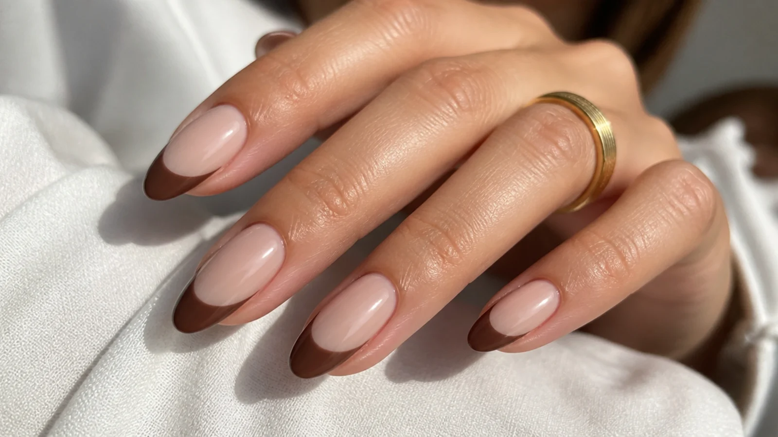 Medium almond nails with chocolate brown French tips over a sheer nude base