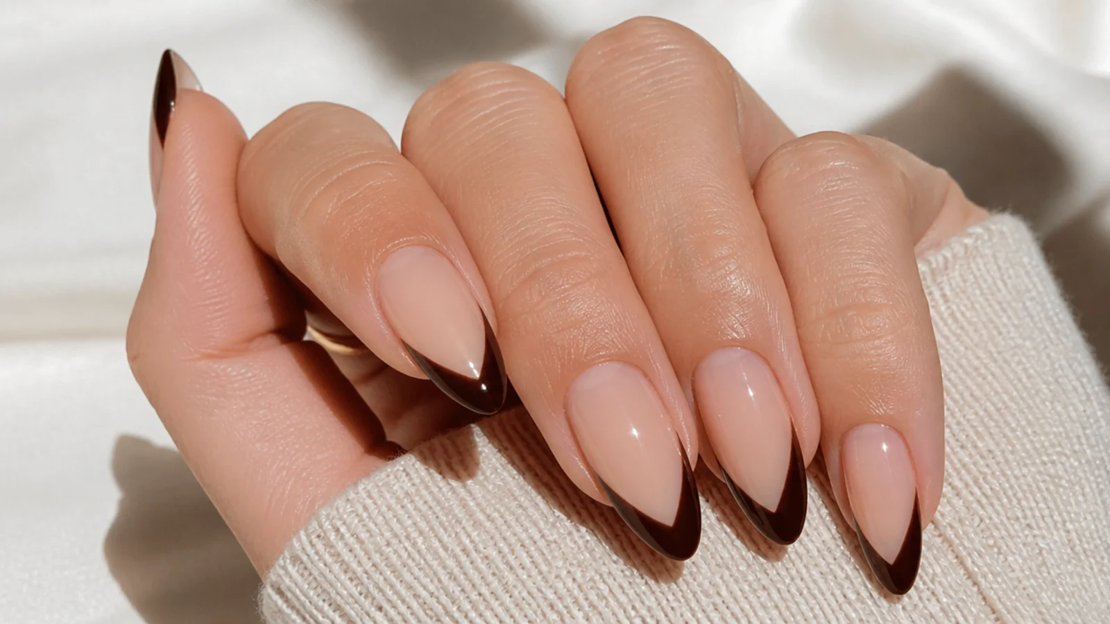 Long almond nails with a chocolate brown V-shaped French tip over a nude base