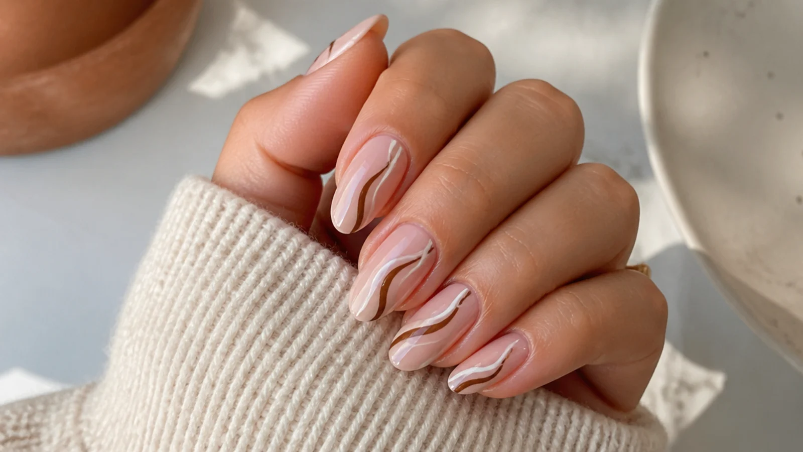 Medium almond nails with wavy brown and cream swirl lines on a nude base