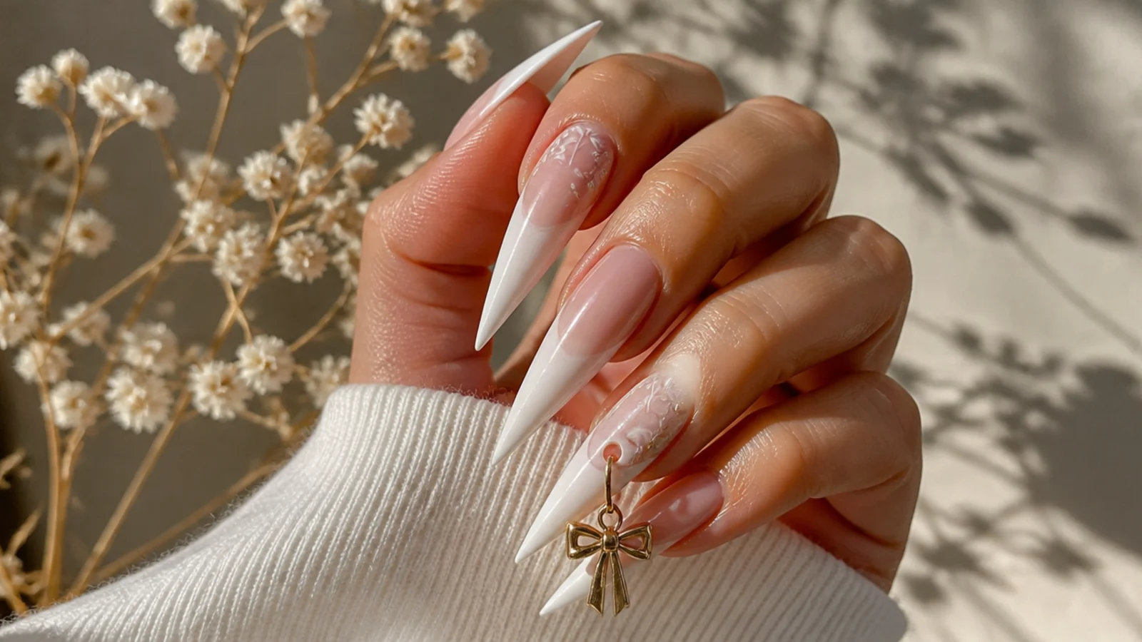 Long stiletto nails with a dangling metal charm threaded through a drilled nail piercing
