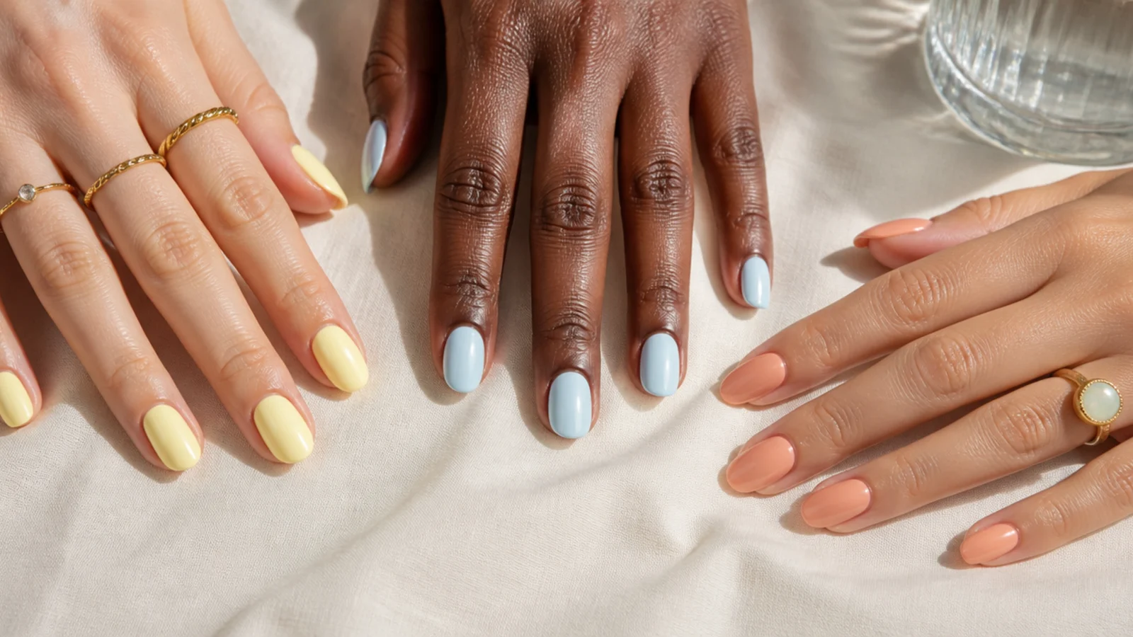 Three hands with different skin tones wearing butter yellow, baby blue and peach pastel nails