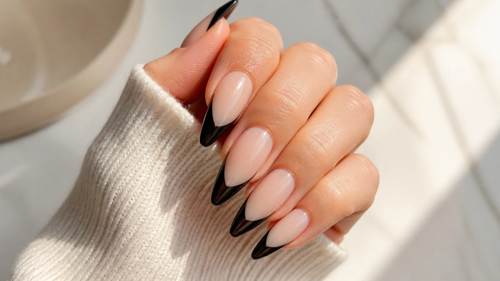 Stiletto nails with a sharp black French tip over a sheer nude base