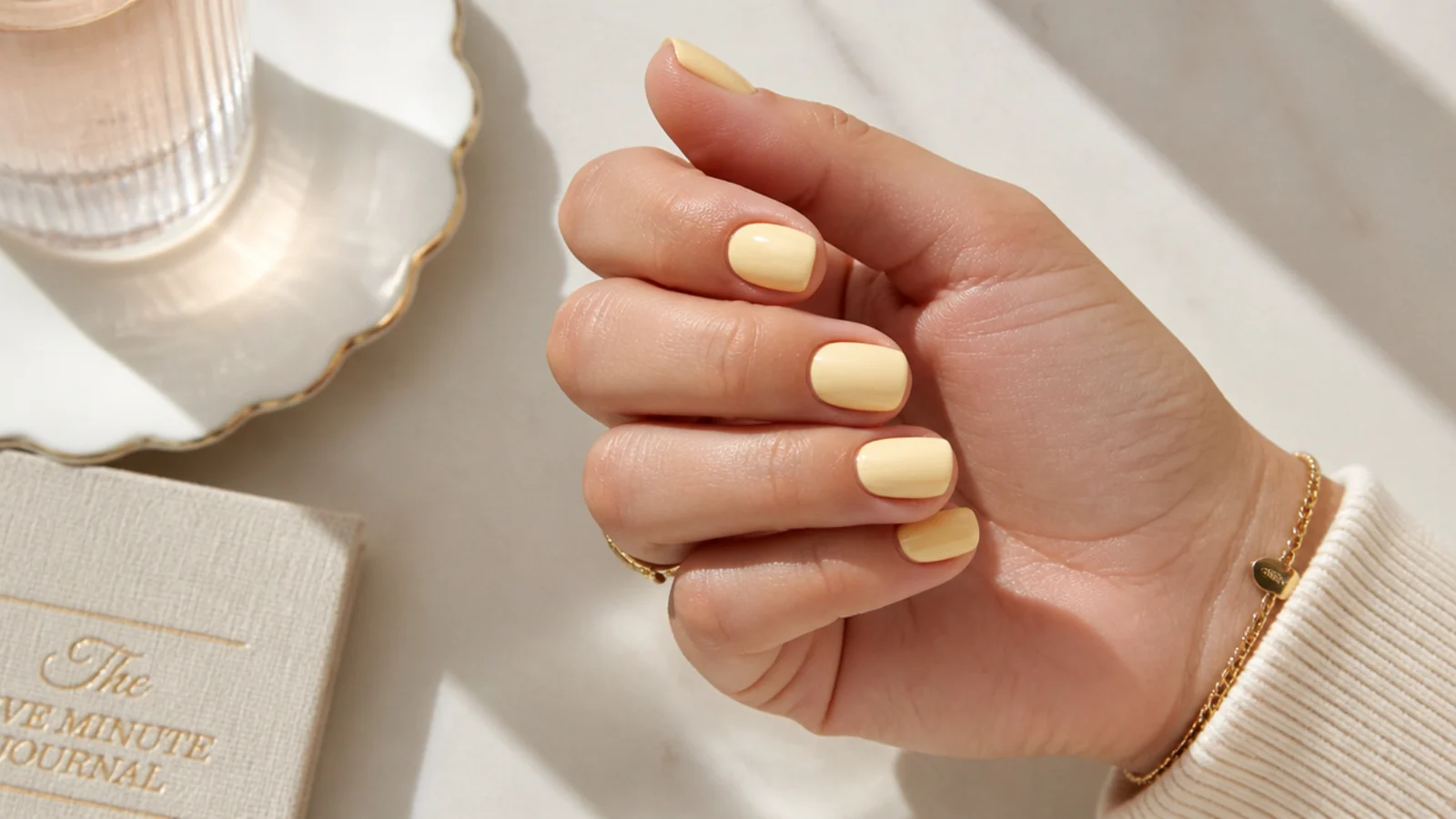 Short glazed butter yellow summer nails with a glossy finish on a sunlit table