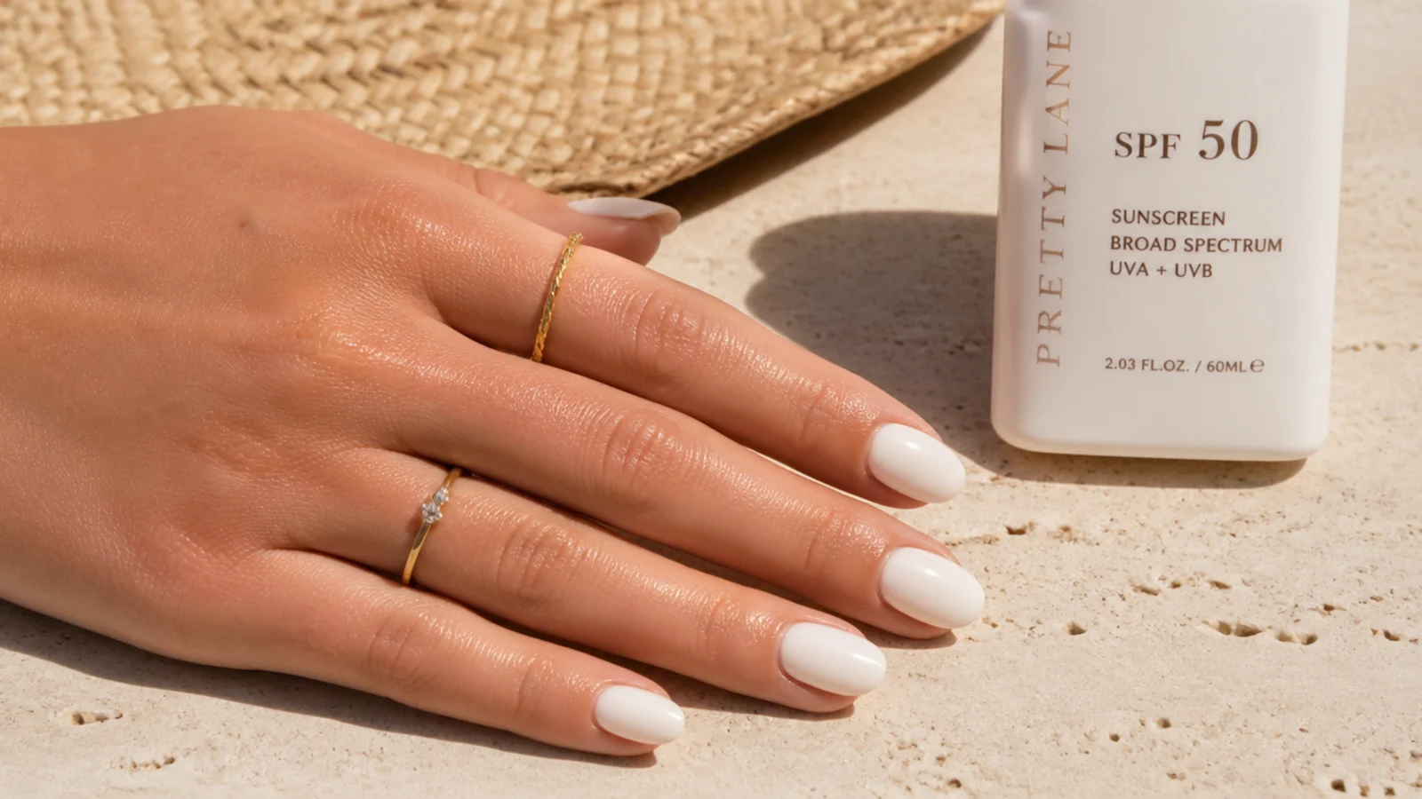 Bottle of sunscreen beside a hand with milky white summer nails