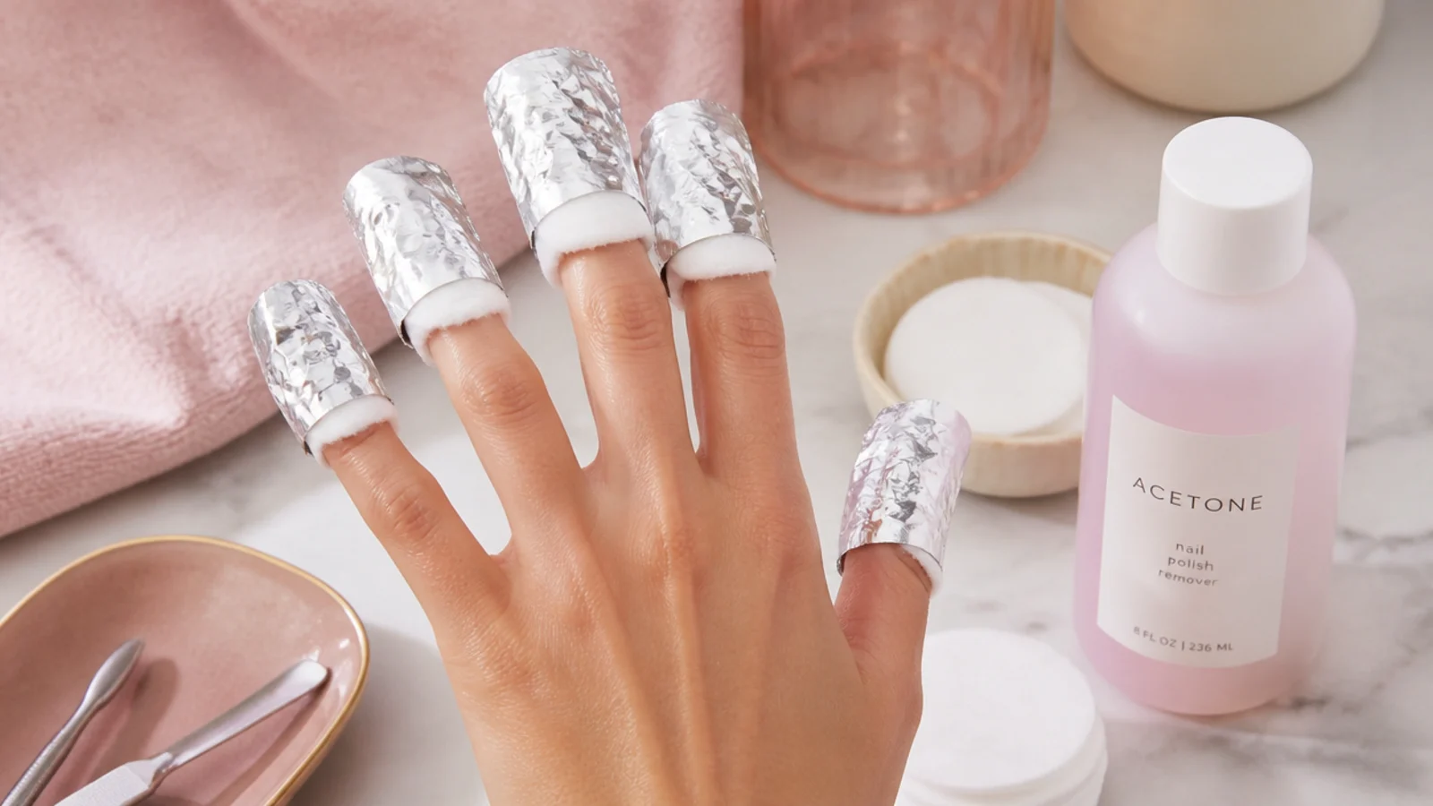 Hand with cotton pads and foil wraps soaking acrylic nails in acetone for safe removal