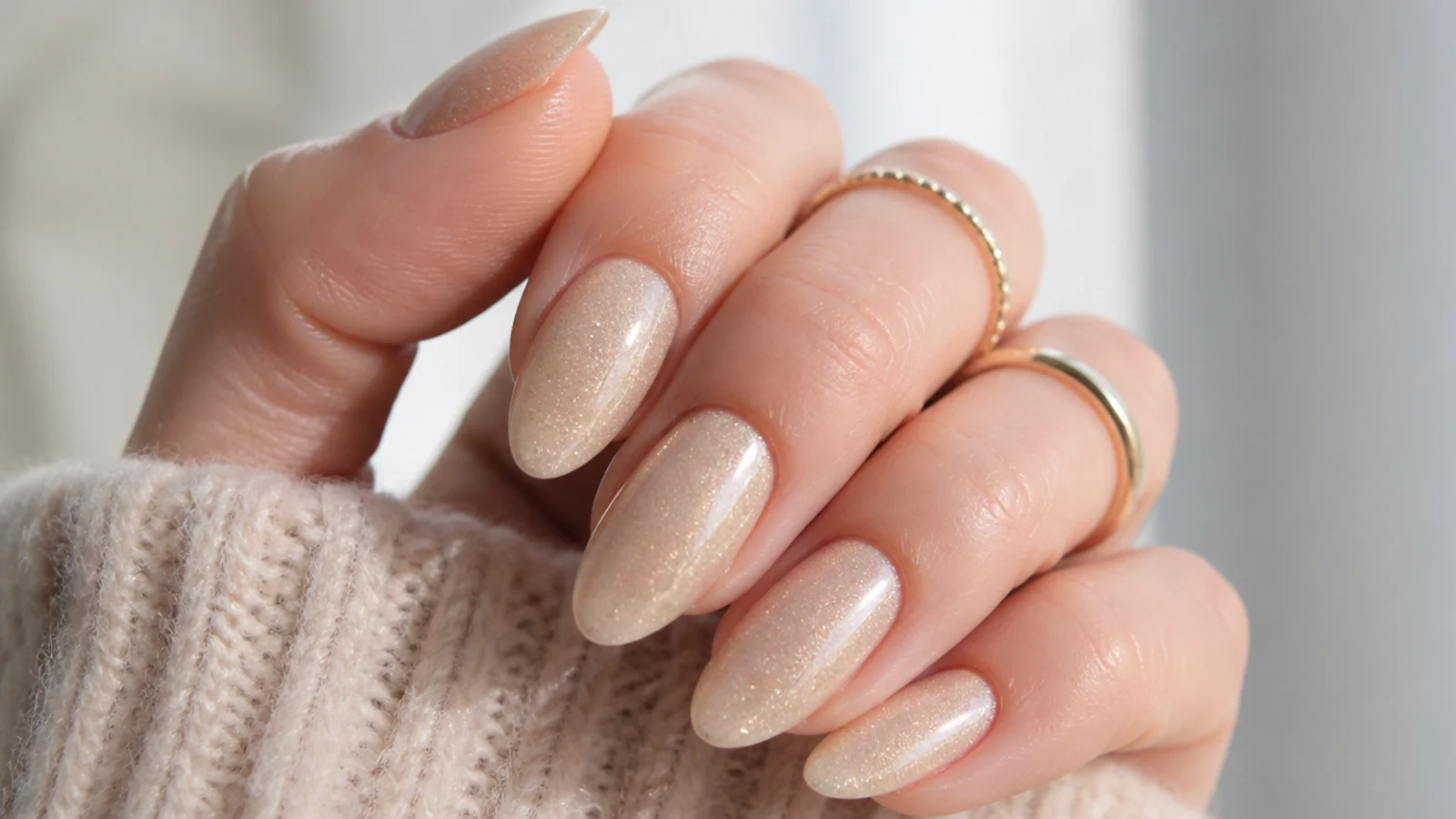 Almond nails in champagne beige with fine gold micro shimmer catching the light