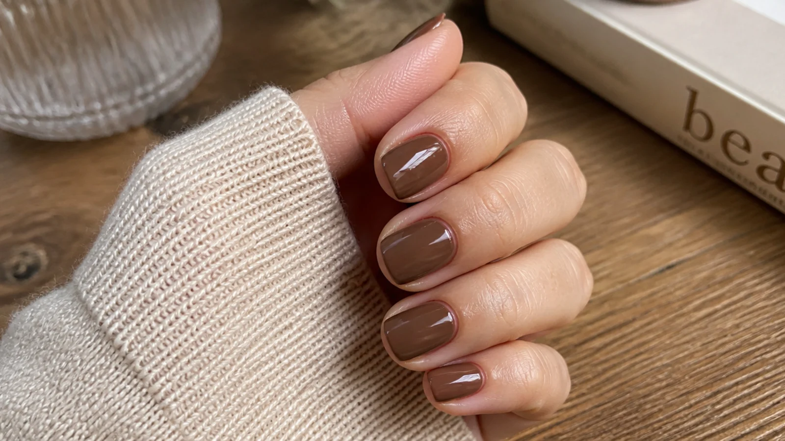 Short squoval nails in mocha brown gel with a glossy finish on a wooden desk