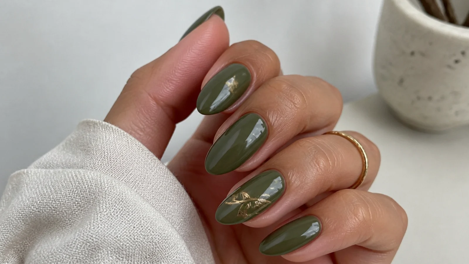 Earthy olive green gel nails in an almond shape on tan hands at home