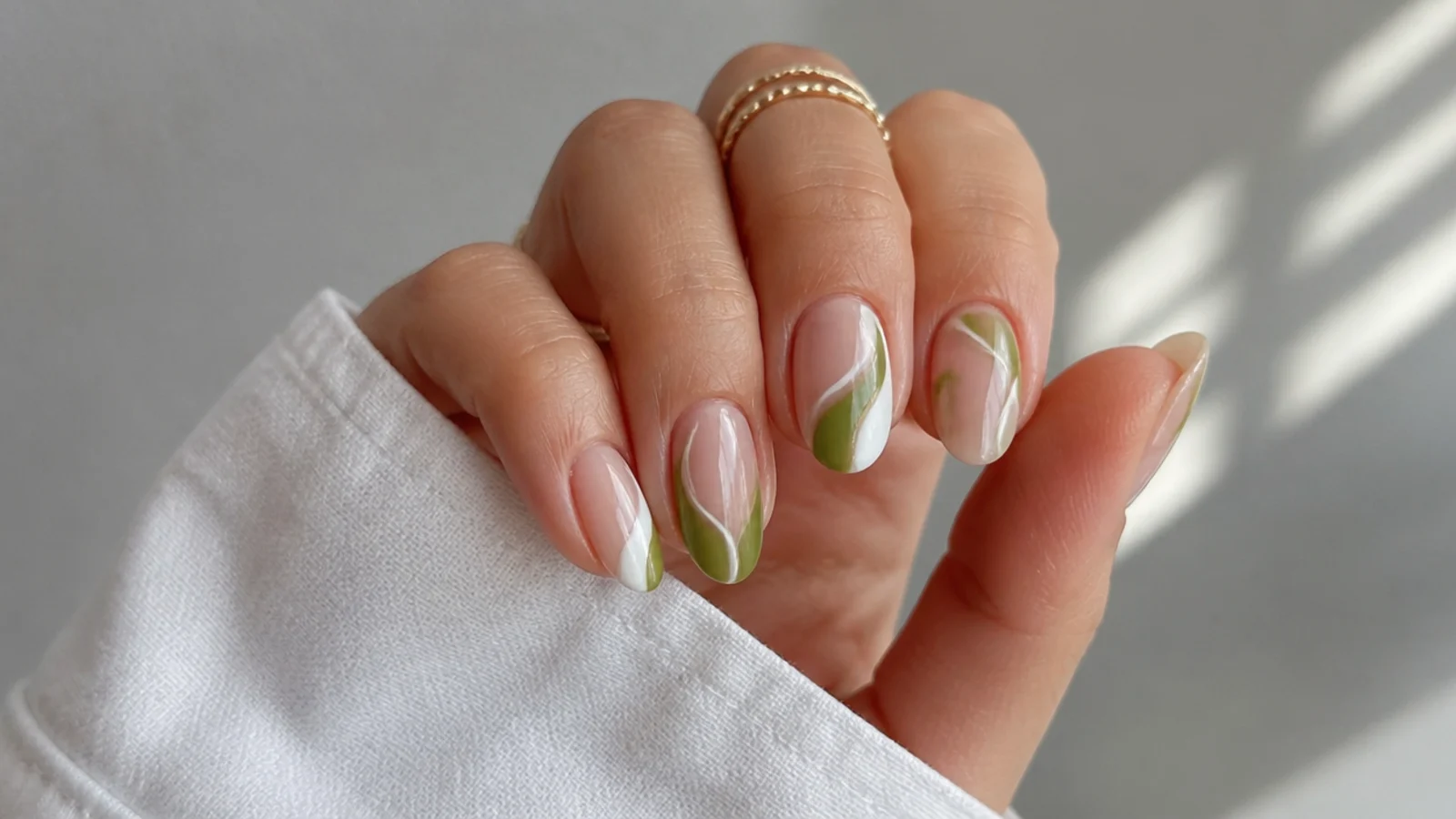 Negative-space nails with olive green and white shapes on bare nail