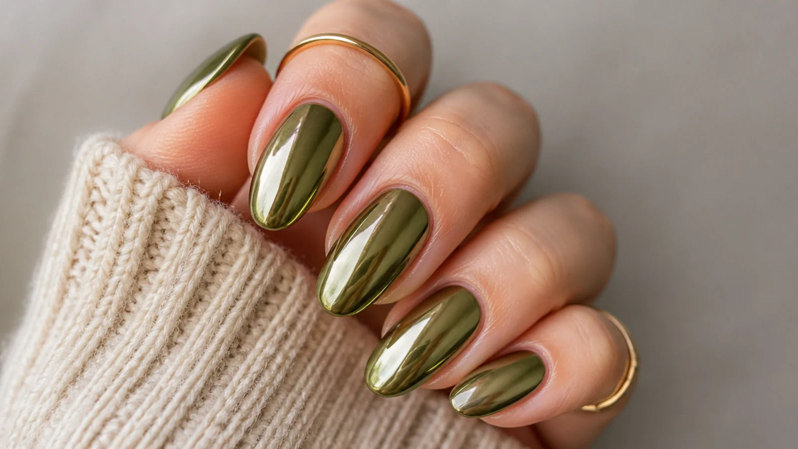 Mirror-finish olive green chrome nails on an almond shape catching warm light