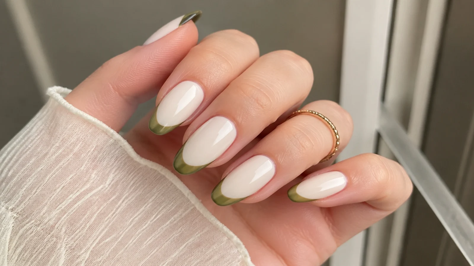 Almond nails with a cream base and thin olive green french tips