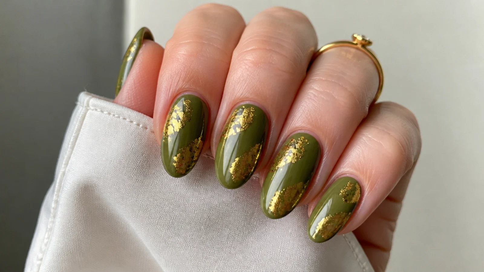 Olive green nails with gold foil flakes on an almond shape