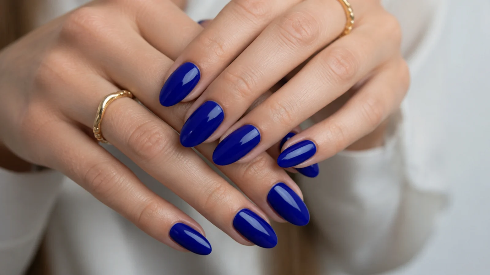 Glossy true royal blue gel nails in an almond shape on manicured hands